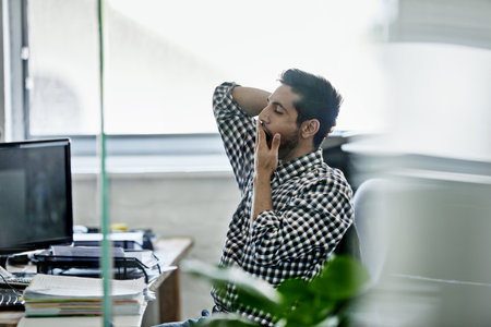 This is hard work. a handsome young designer yawning while working on a pc.の写真素材