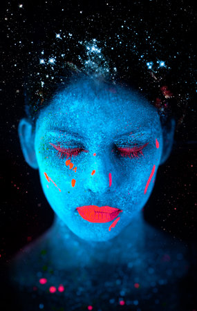Galactic beauty. a young woman posing with neon paint on her face.