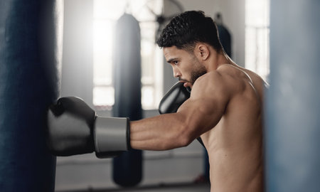 Training, fitness and workout man boxer, sweating and doing a cardio exercise at the gym. Sporty, sweaty and determined male athlete punching a bag at a sports boxing center for health and wellnessの写真素材