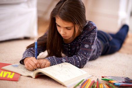Shes a budding young artist. A young girl coloring while lying on the floor.