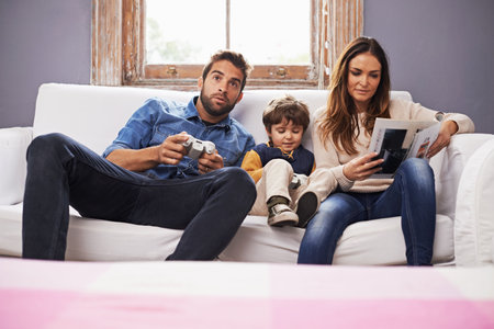 Time with family is time well spent. a son and his father playing a video game together while his mother reads a magazine.の写真素材