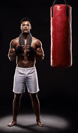 Practice and improve everyday. Studio shot of kick boxer working out with a punching bag against a black background.の写真素材