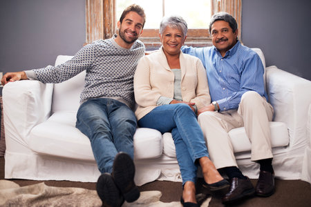 They are still the ones I run to...Portrait of a happy couple sitting with their adult son at home.