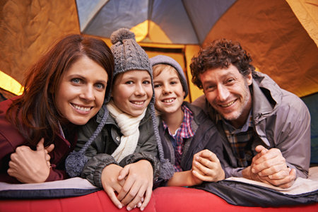 Family camping is family bonding. Portrait of smiling family of four relaxing in tent on a camping holiday.の写真素材