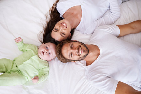 He always wants to be close to mommy and daddy. a young couple lying on the bed with their baby boy.