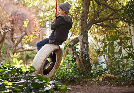 Carefree summer days of an idyllic childhood. A preteen boy swinging on a tyre swing in the garden.