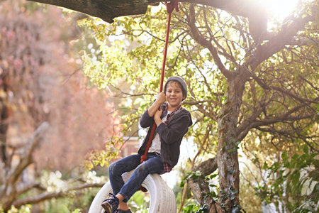 Carefree summer days of an idyllic childhood. A preteen boy swinging on a tyre swing in the garden.の写真素材