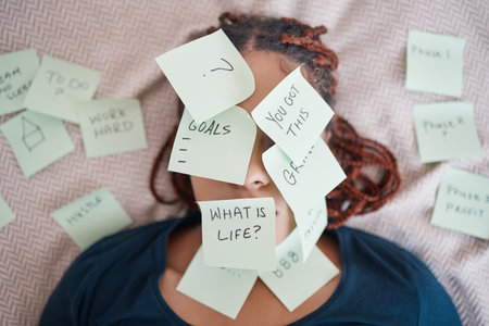 Black woman on bed, sticky note on face for motivation and success in life. African lady in bedroom, stick paper with questions on skin and eyes, planning strategy, for career and personal goalsの写真素材