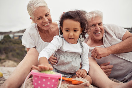 Senior family with girl playing in beach sand together for holiday, outdoor wellness and child development. Grandmother, grandparents care and love for baby or people relax on vacation or retirementの写真素材
