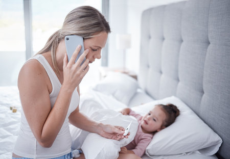 Bed, sick girl and mother phone a doctor feeling stress reading thermometer results. Mom on a mobile call listen and help with child health care for kid in a house bedroom feeling anxiety from covidの写真素材