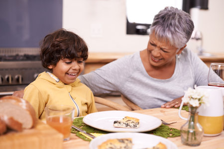 Granny can you teach me how to make this. A cute little boy eating a meal with his grandmother at home.の写真素材