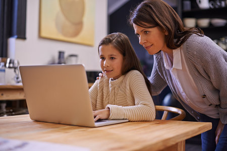 Browsing the internet with mommys supervision. a young girl studying with her mother nearby to help.