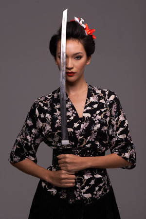 Shes a master with the sword. Studio shot of an attractive young woman holding a samurai sword.の写真素材