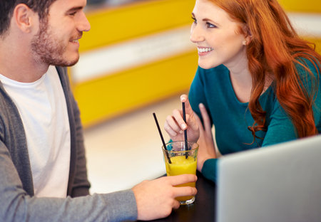 Glad to spend time with each other. A loving young couple drinking orange juice while sitting with a laptop in a cafe.の写真素材