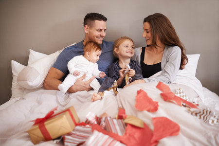 Thanks mommy and daddy. an affectionate young family lying in bed and exchanging gifts.の写真素材