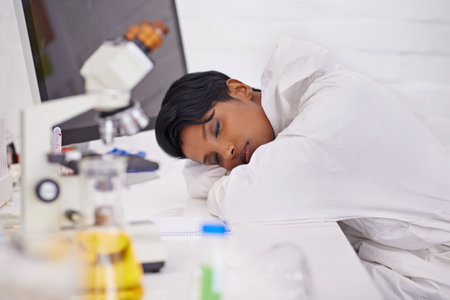 Shes a hard worker. A beautiful young scientist napping on her desk in her lab.の写真素材