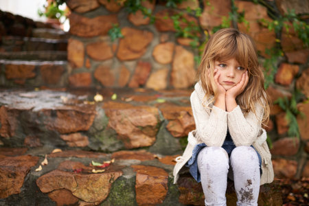 Loneliness strikes. A cute little girl looking lonely while sitting outside on an autumn day.の写真素材