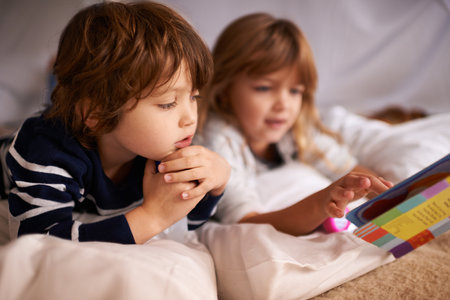 Fairytales under the fort. two adorable siblings using torches to read a book inside their blanket fort.の写真素材