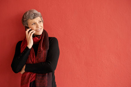 On the phone with her family. a beautiful senior woman talking on her mobile phone in front of a red...