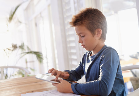 This makes learning so much better. a young boy using a digital tablet to do his homework.の写真素材