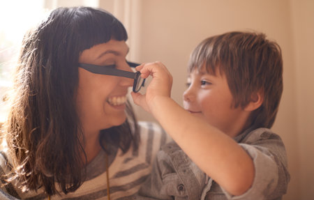 I want to see the world through your eyes...A little boy sitting with his mother and taking her glasses off.の写真素材