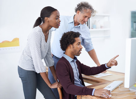 Hes full of incredible ideas. A team of coworkers standing around a computer and discussing a...