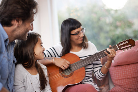 Mommys got the guitar. a woman playing the guitar while sitting with her family.の写真素材