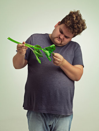 What is this thing. an unhappy overweight man holding a celery stick.の写真素材