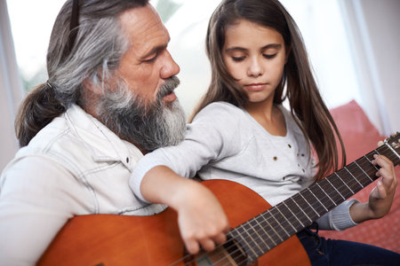 Getting guitar tips from a seasoned musician. a little girl playing guitar with her grandfather.の写真素材