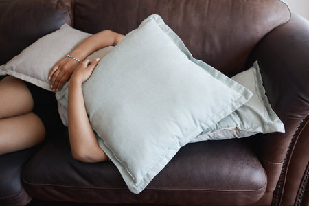 Tired, depressed girl sleeping under pillow on sofa in the living room. Woman hide feeling sad or...