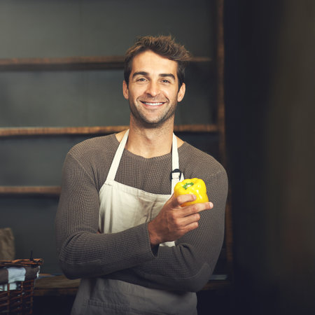 Veggies full of flavor. a young man holding a yellow pepper in his kitchen.