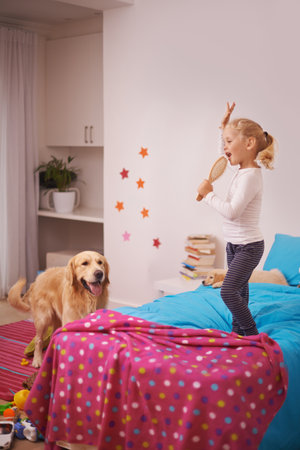 A star in the making. A little girl jumping on her bed and singing into her hairbrush while her dog watches.の写真素材