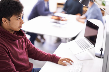 Hes fully focused in the office. a young man working on his laptop in an office.
