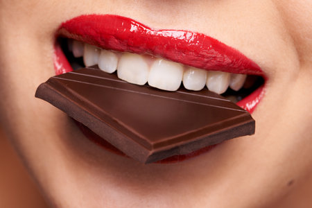Every woman needs a guilt-free chocolate day. Closeup portrait of a cute young female biting on a chocolate bar.の写真素材