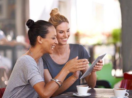 Two young women looking at a tablet in a coffee shop.の写真素材
