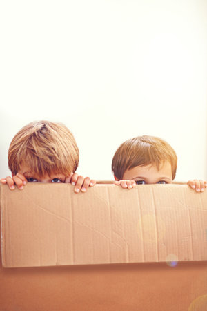 Two adorable young boys peeking out of a cardboard box.の写真素材