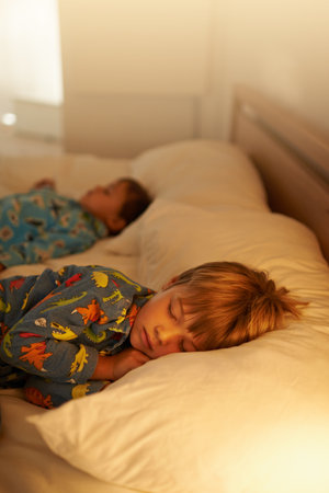 Tuckered out after a day full of fun. two little boys sleeping on a bed with the light on.