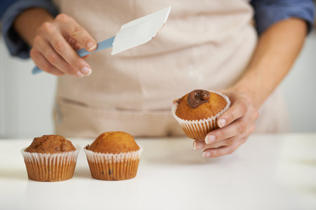 Whats a cupcake without some frosting. A closeup image of a woman applying frosting to a cupcake.の写真素材