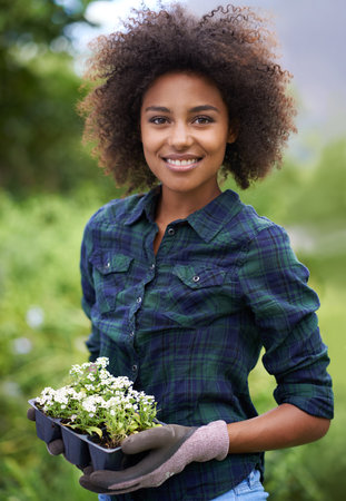 Proud plant parent. Portrait of a happy young woman holding a tray of seedlings in a garden.の写真素材