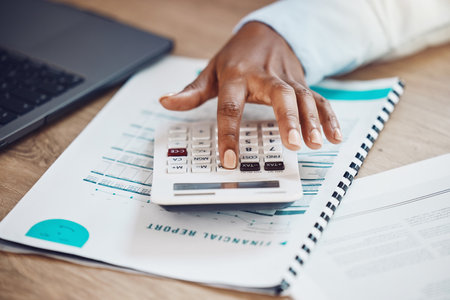 Hand of a woman working on a financial report with a calculator at her desk in the office. Professional accounting manager calculating the company finance budget, documents or bookkeeping paperwork.の写真素材
