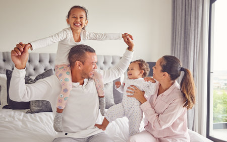 Comic family, happy and bedroom portrait while relax in home together, smile for parents love and international hotel holiday. Excited kids with mother and father on holiday and being playful in bedの写真素材
