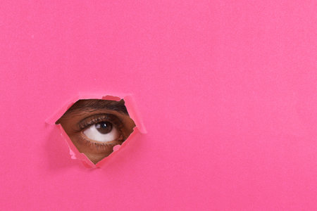A view of a mans eye looking through a hole in some colorful paper.の写真素材