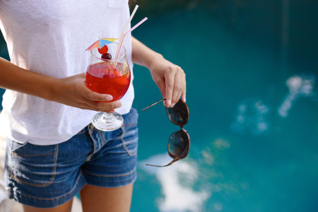 young woman standing by a swimming pool with a cocktail in her hand.の写真素材