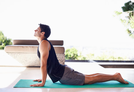 A side view shot of a content young man doing yoga at home.