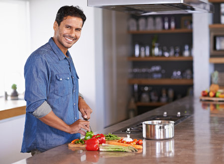 I insist on the healthiest ingredients. Cropped view of a handsome young man chopping vegetables.の写真素材