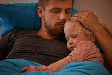 Devoted to his little girl. A little girl asleep in her fathers arms in bed.の写真素材