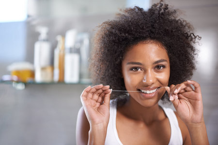 For a bright smile. a young woman flossing her teeth in the mirror.