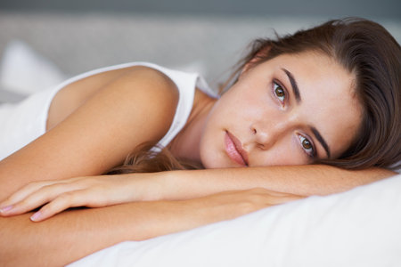 Theres a lot on my mind today...A beautiful young woman looking sad while lying on her bed.の写真素材