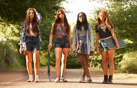 On your marks, get set....Four teenage girls standing outdoors with their skateboards.