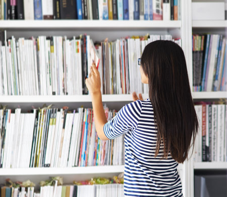 Some books you find, others find you. a woman browsing through a bookshelf at home.